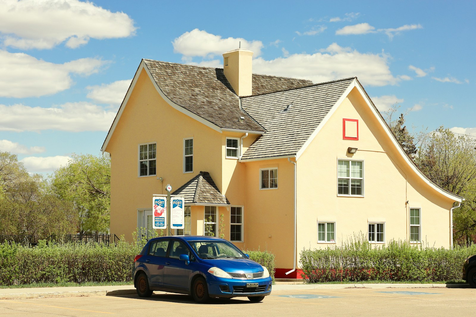 A yellow house sits beside a blue car.
